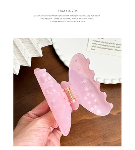 Close-up of a pink translucent butterfly hair claw clip with pearl accents held by a hand