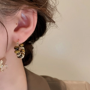 Detailed close-up of vintage golden hoop earrings with brown tiger eye beads on model