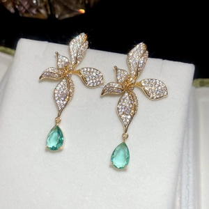 Detailed macro of 18k gold earrings with zircon flowers and green teardrop gems