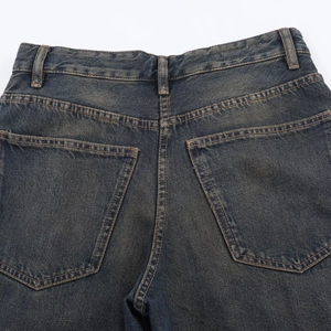 Detalle de los vaqueros azul oscuro con lavado vintage, bolsillos traseros y costuras amarillas