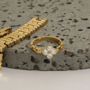 Macro shot of gold four-leaf clover ring with zircons on gray volcanic rock