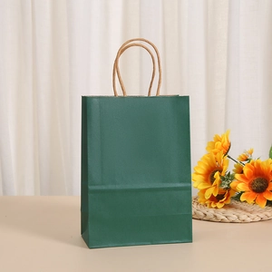Detail of dark green kraft paper gift bag with twisted handles in a cozy home setting