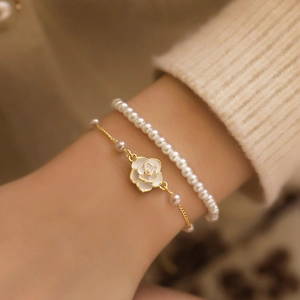 Detail view of a camellia flower pendant and pearl bead layered bracelet on a female wrist