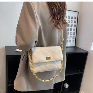 White quilted shoulder bag with gold chain strap shown on a model for scale and style