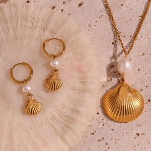 Close-up of golden shell jewelry set with pearls on white coral stone background