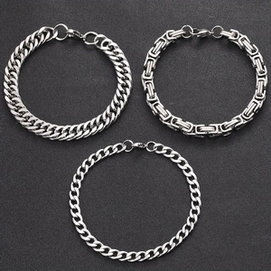 Three silver-tone hip hop cuban and byzantine chain bracelets on dark grey surface