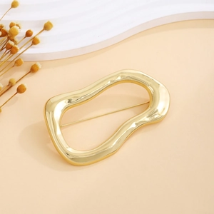Irregular oval golden brooch with glossy finish on a minimalist decorative background