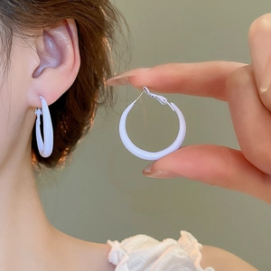 Close-up of a woman wearing white glossy hoop earrings with a minimalist circular design