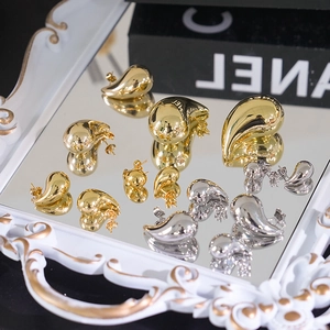 Polished gold and silver teardrop earrings displayed on a white decorative mirror