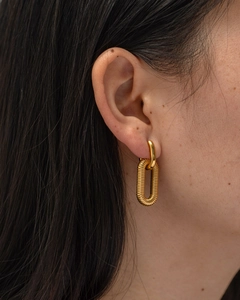 Macro shot of gold chain link earrings featuring a textured industrial spring pendant detail