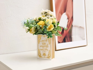 Creative book-shaped ceramic vase in white with gold script and artificial flowers