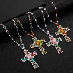 Close-up of gold and silver necklaces with colorful rhinestone cross pendants on dark base