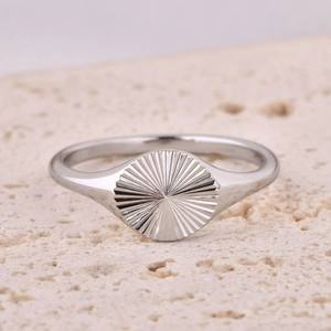 Close-up of silver sunburst signet ring on natural stone showing modern texture