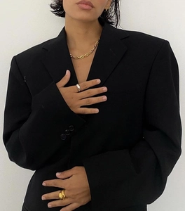 Dettaglio di una catena in oro 18k e anelli abbinati a un blazer nero elegante