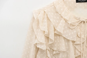 Close-up of beige tulle blouse featuring layered ruffles and textured polka dot details
