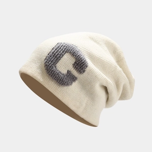 Detailed close-up of gray bouclé embroidered C letter on cream knitted beanie