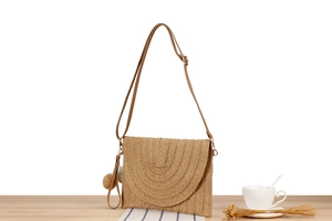 Detail of hand-woven straw shoulder bag with decorative tassels on wooden table