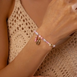 Detail of pink beads and pearl bracelet with conch shell charm and tassel on wrist