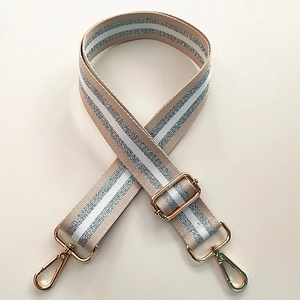 Detail of adjustable beige bag strap featuring silver glitter stripes and gold metal hooks
