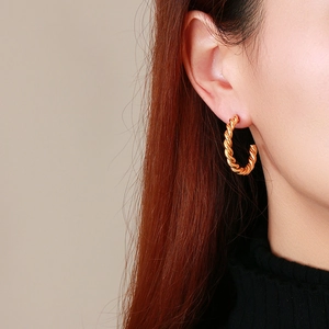 Close-up of gold-finished C-shaped hoop earrings with a stylish twisted rope texture