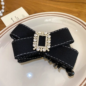 Barrette à nœud en tissu noir élégante avec strass brillants sur une assiette blanche