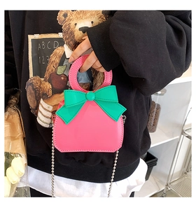 Pink mini leather handbag featuring a contrasting green bow and silver chain strap details