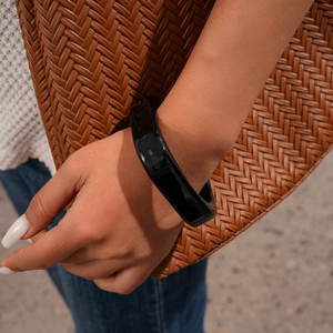 Close-up of polished black resin bangle worn with a stylish woven texture handbag