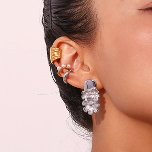 Macro shot of gold ear cuffs and silver floral pendant earrings worn as a stylish set