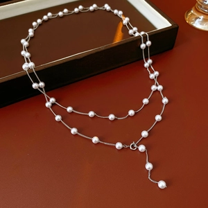 Detail of layered white pearl necklace with silver chain on premium brown leather surface