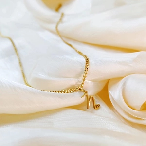 Macro detail of gold letter n pendant with tiny heart on luxurious silk background