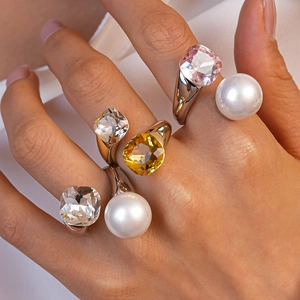 Detail of stacked irregular square crystal and pearl rings on a hand in golden and silver finish