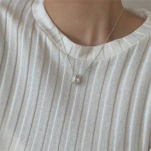 Detail of silver hollow spherical pendant necklace worn on a white knit sweater