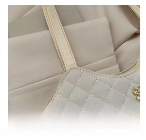 Détail d'un sac cabas beige avec coutures en losanges et logo floral métallique doré