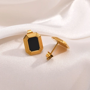 Detailed macro view of gold-plated square black agate earrings on white silk