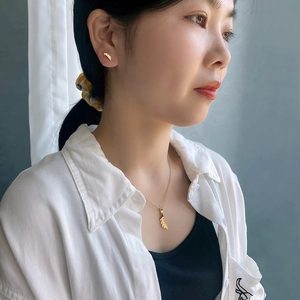 Close-up of a model wearing golden leaf-shaped stainless steel necklace and stud earrings