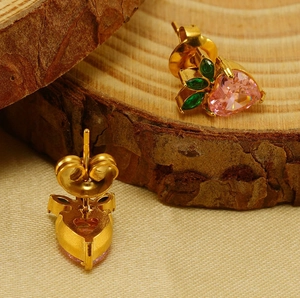 Macro shot of pink heart gemstone and green leaf stones on a gold fruit-shaped earring