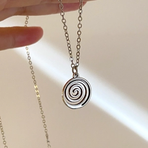 Collier avec pendentif spirale argenté tenu à la main sur un fond lumineux épuré