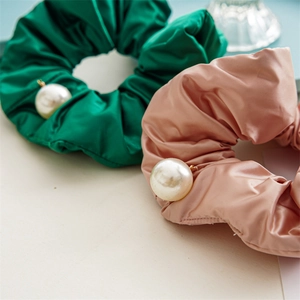 Detailed shot of green and pink satin scrunchies with elegant pearl embellishments