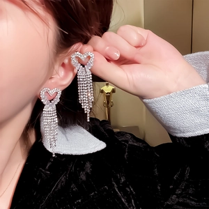 Close-up of sparkling zircon heart tassel earrings on model showing elegant drape
