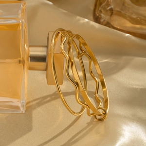 Three-piece stackable gold wave geometric bracelets draped over a luxury perfume bottle