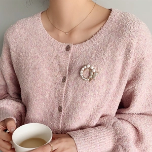 Detail of round pearl butterfly brooch pinned on a pink knit cardigan for women