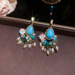 Detail of drop earrings with turquoise stones, pearls and tassels on leather background