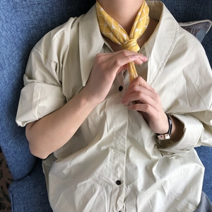 Detailed view of yellow plaid cotton linen scarf tied elegantly on a beige shirt