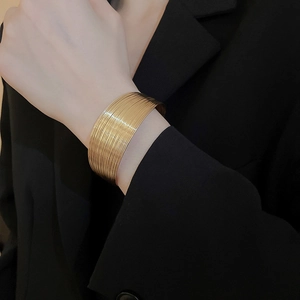 Detailed view of a wide gold-tone textured cuff bracelet worn on a model's wrist