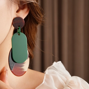 Close-up of geometric resin earrings in amber and green tones on a female model