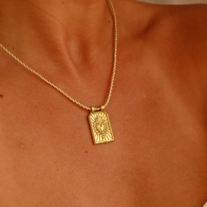 Macro view of a gold tarot-style pendant featuring a flaming heart on a braided cord