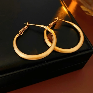 Detailed macro view of matte gold hoop earrings resting on a black leather jewelry box