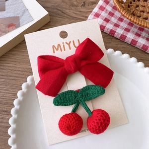 Détail d'un nœud en velours rouge et barrettes cerises au crochet sur plat blanc
