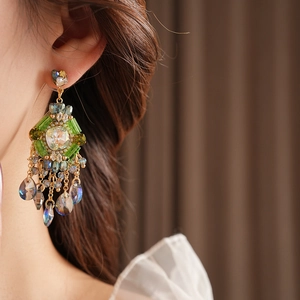 Detail of bohemian gold earrings with green crystals and teardrop tassels worn by a model