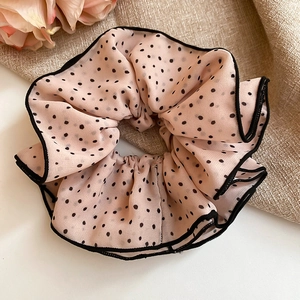Detailed close-up of pink polka dot chiffon scrunchie with layered lace edges on fabric